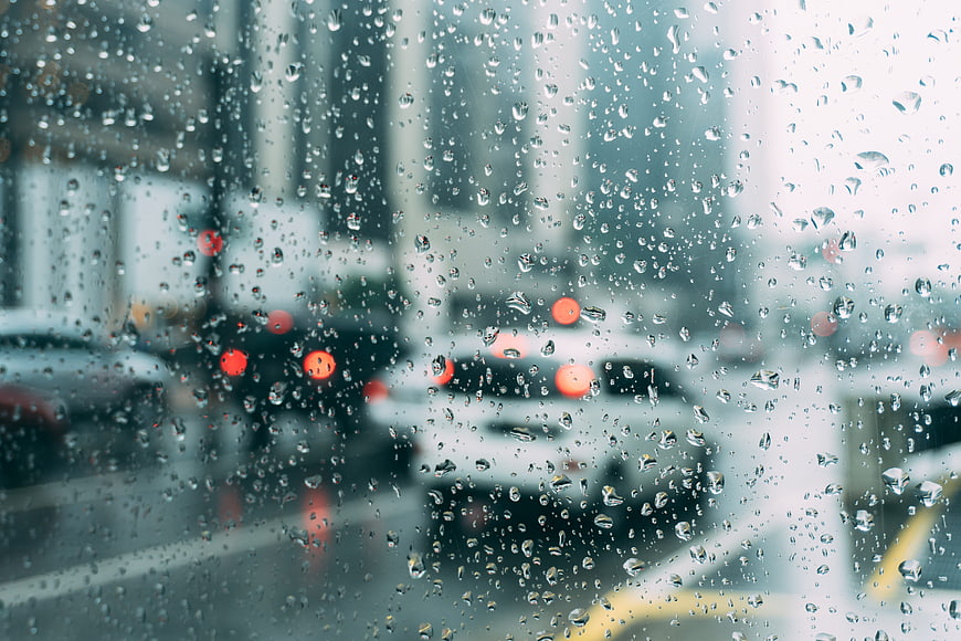 Raindrops on glass window with blurred city traffic and red car lights