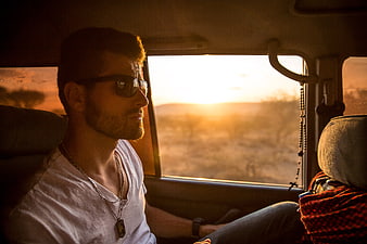 Man with sunglasses looking out car window at sunset