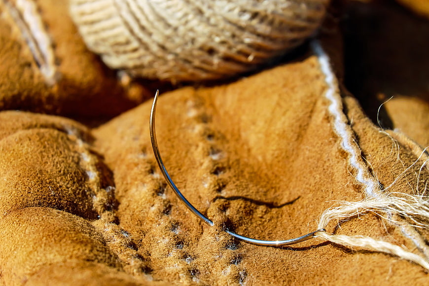 Close-up of curved needle stitching brown leather with twine