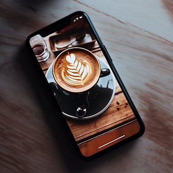 Smartphone displaying latte art coffee photo on wooden table