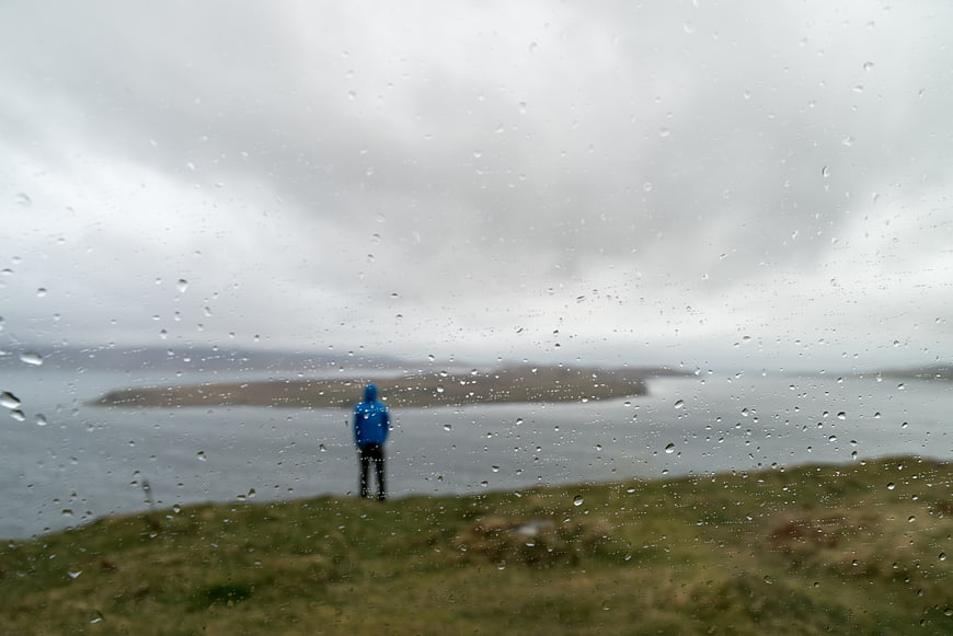Lone figure in blue jacket looking at island through raindrops