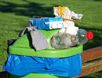 Overflowing green trash bin with plastic bottles and waste