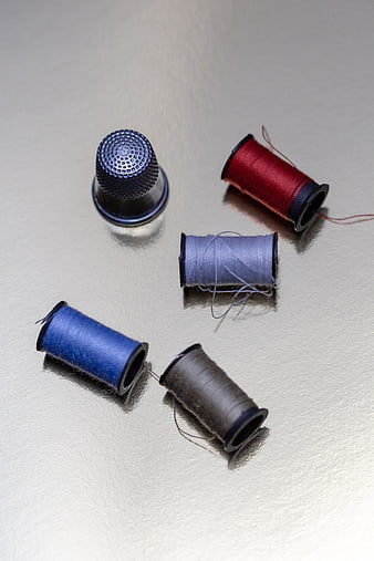 Colorful thread spools and metal thimble on white surface
