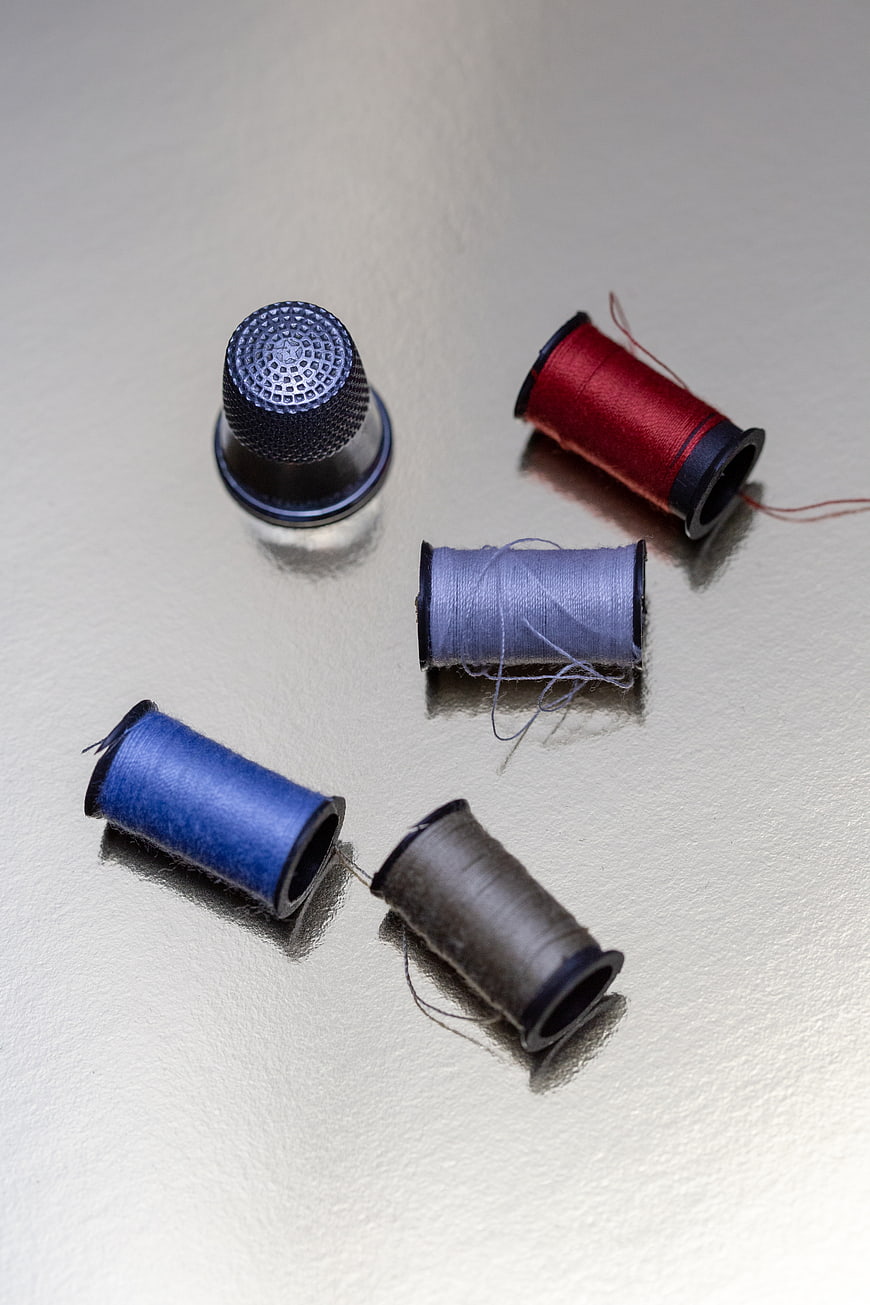 Colorful thread spools and metal thimble on white surface