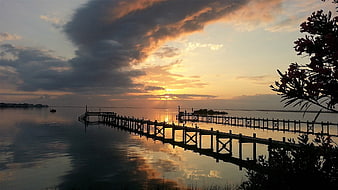 Sunset over a wooden pier on a calm bay with dramatic clouds