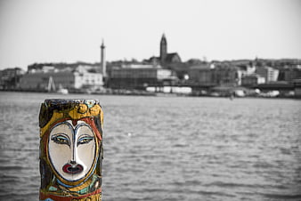Painted wooden sculpture face on riverbank with Gothenburg city skyline in background