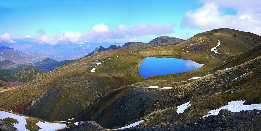 Panoramic mountain landscape with alpine lake and snow patches