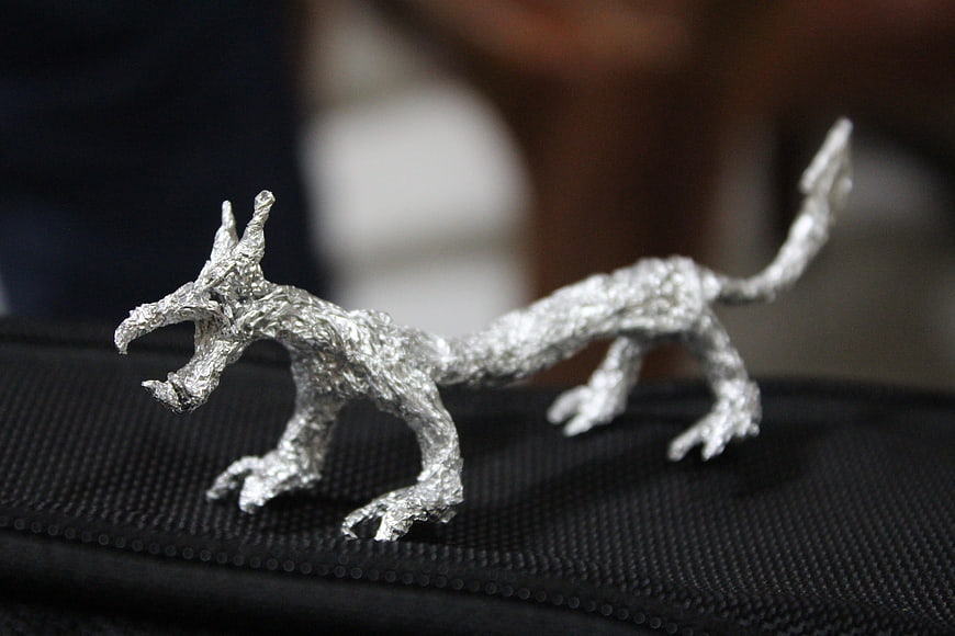 Handmade silver foil dragon sculpture on black textured surface