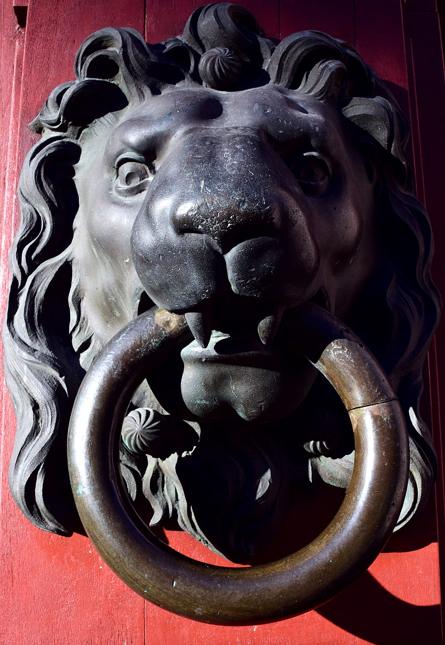 Close-up of antique bronze lion head door knocker on red door
