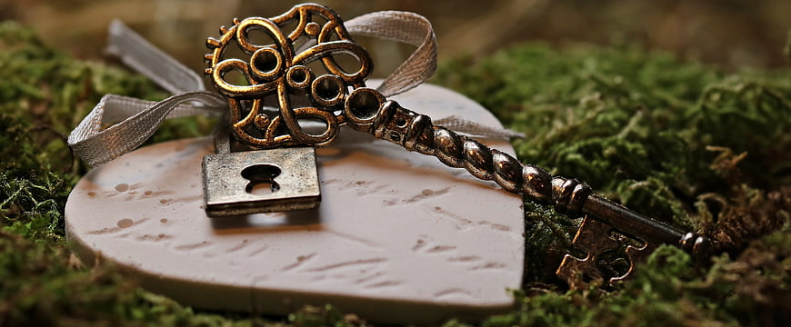 Vintage ornate key and padlock on heart-shaped stone with moss
