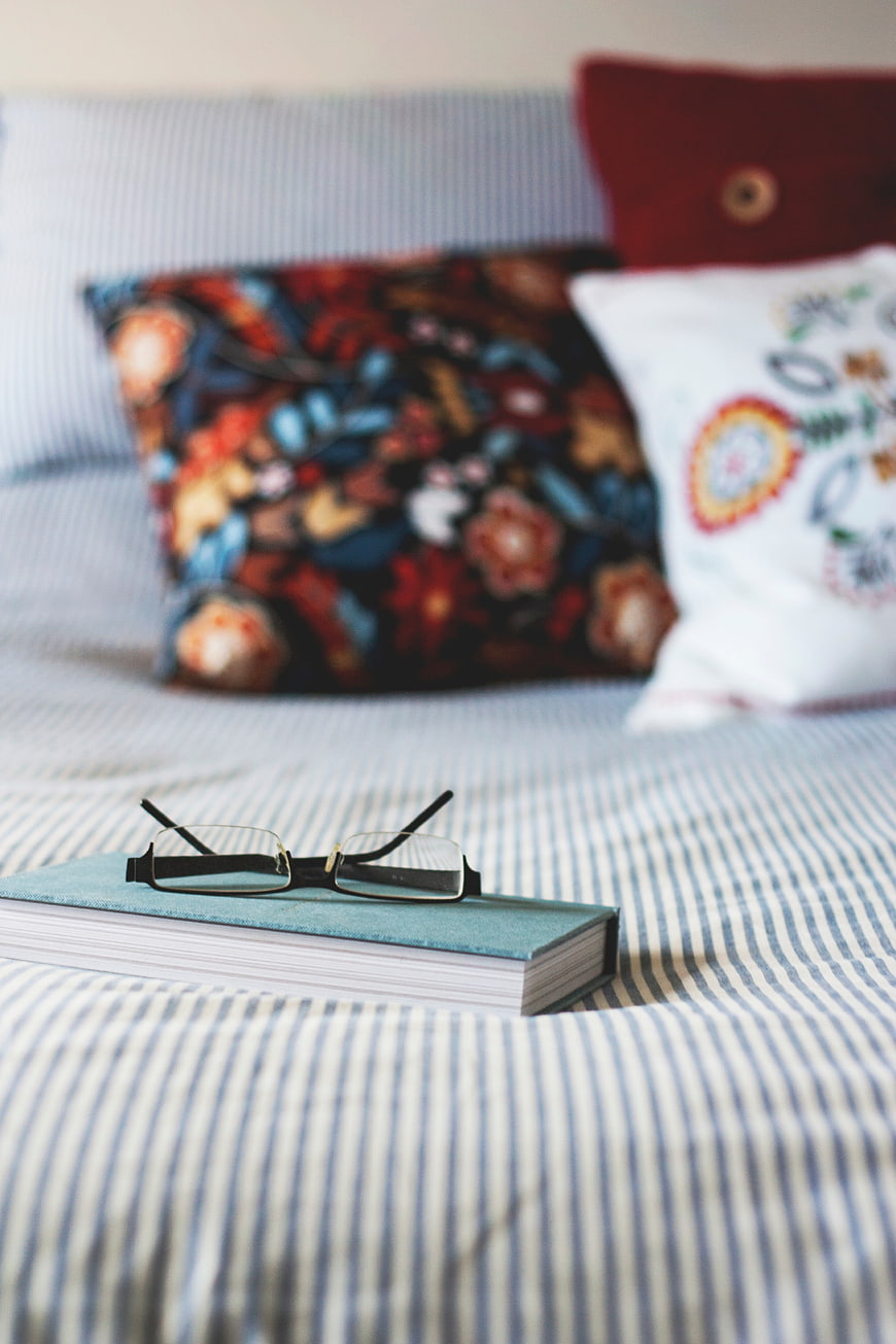 Reading glasses on a book on a striped bed