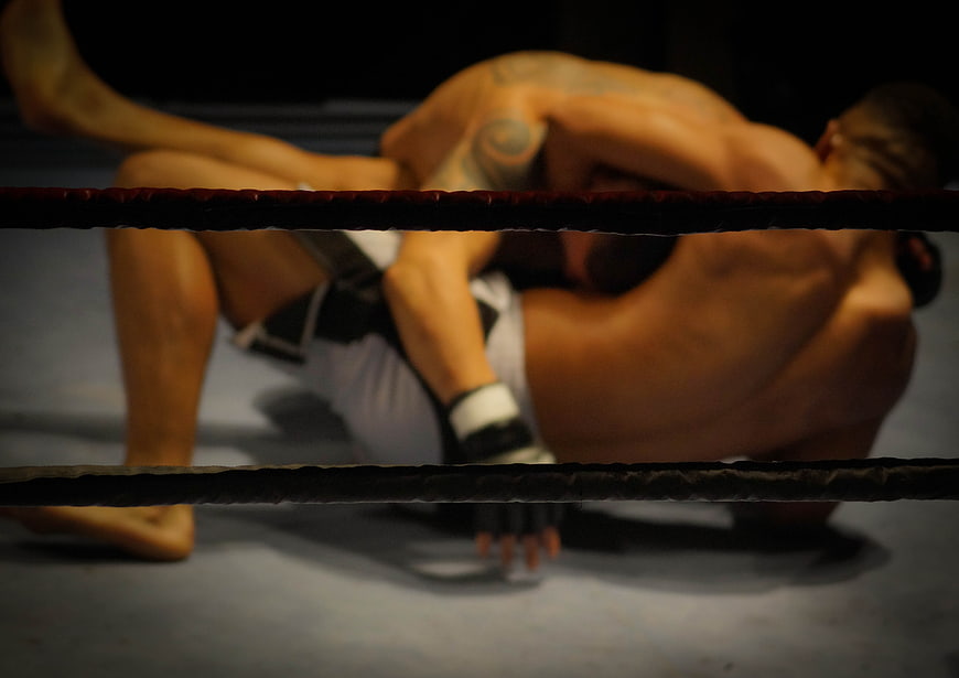 MMA fighters grappling in a boxing ring viewed through ropes