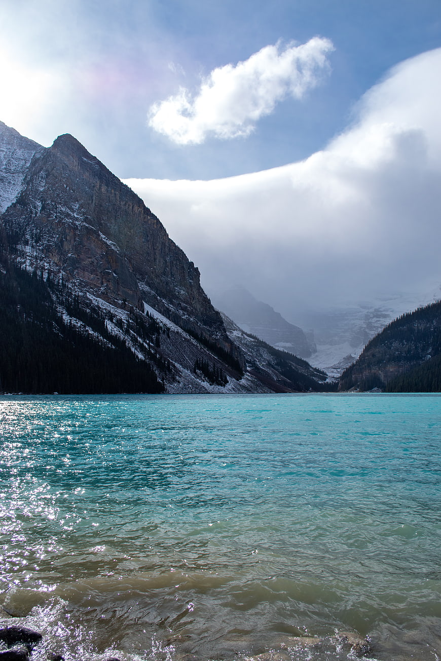 Turquoise glacial lake with snow-capped mountains and clouds