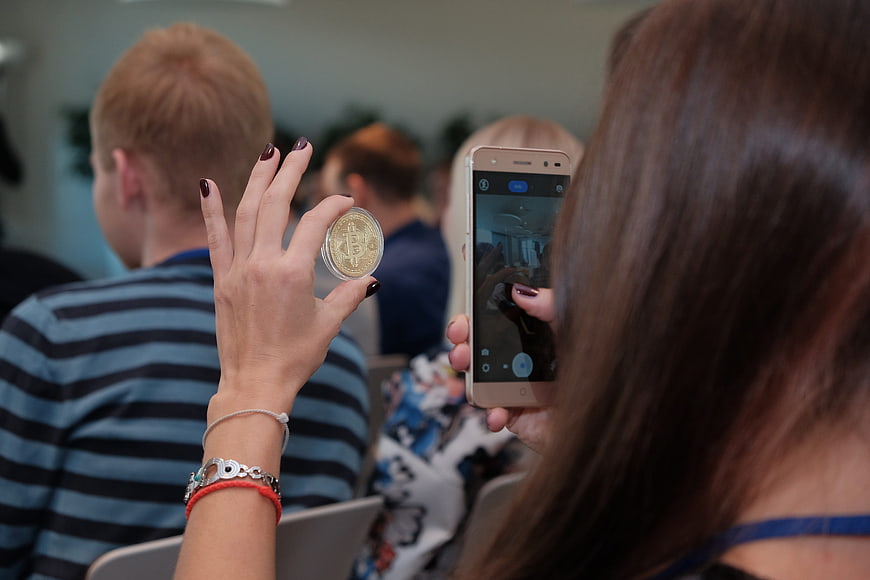 Woman photographing physical Bitcoin coin with smartphone