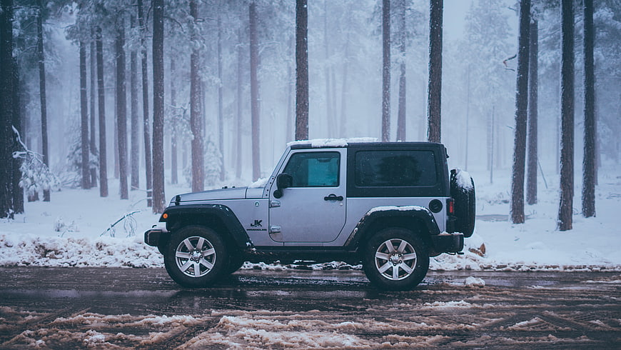 White Jeep Wrangler parked on snowy forest road