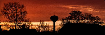 Silhouette of water tower and trees against dramatic red sunset sky
