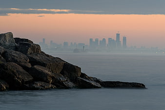 Rocky Shoreline with Hazy City Skyline at Dusk