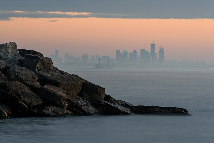 Rocky Shoreline with Hazy City Skyline at Dusk