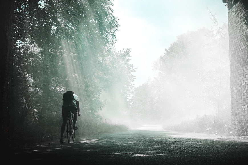 Cyclist Riding Through Misty Forest Road with Sun Rays