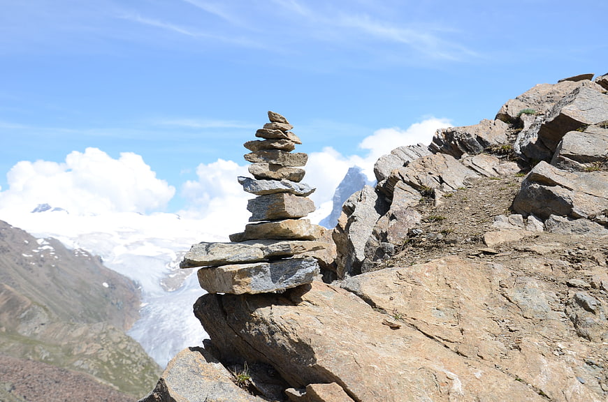 Stacked stone cairn on rocky mountain peak with glacier background
