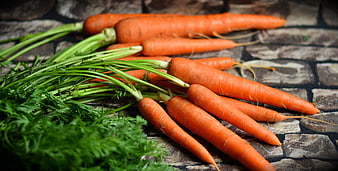 Fresh raw carrots with green tops on rustic stone background