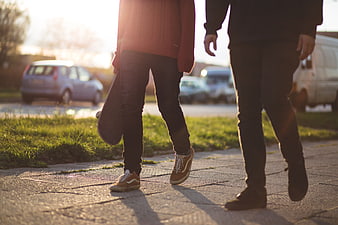 Two friends walking on sidewalk with skateboard at sunset