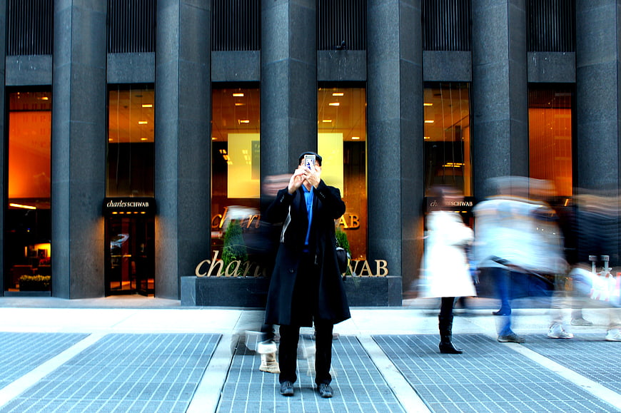 Man taking photo with smartphone in front of Charles Schwab building