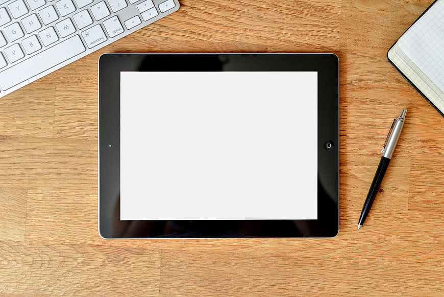 Top view of tablet with blank screen on wooden desk