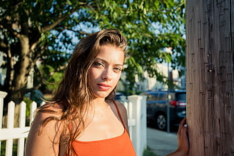 Young woman leaning against wooden post in sunlight