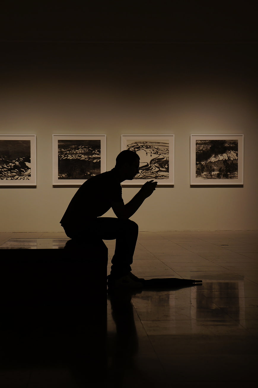 Silhouette of man sitting in dark art gallery viewing paintings