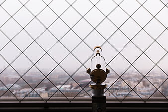 Coin-operated telescope behind diamond wire mesh overlooking city