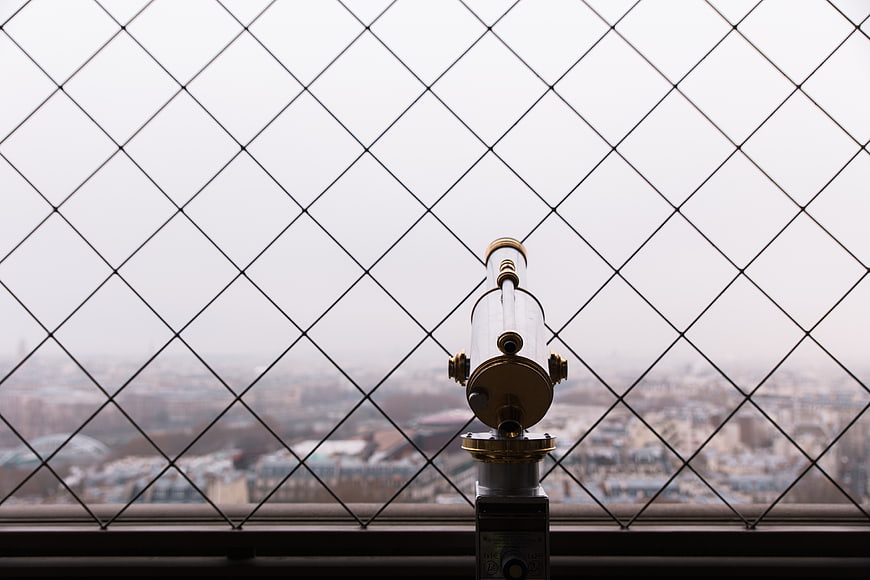 Coin-operated telescope behind diamond wire mesh overlooking city