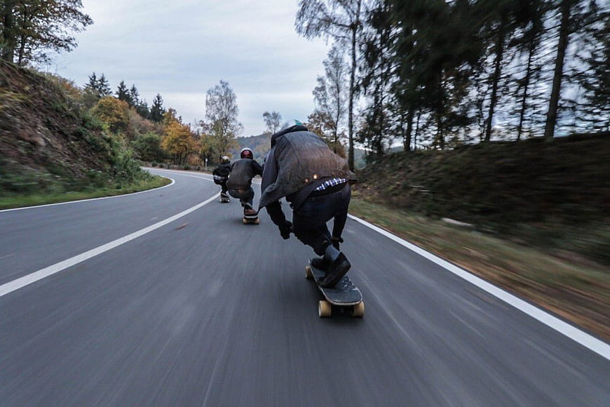 Skateboarders Downhill on Winding Forest Road