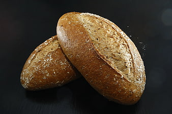 Two loaves of rustic artisan bread on dark background