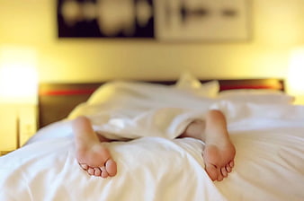 Relaxed feet sticking out from white duvet on bed