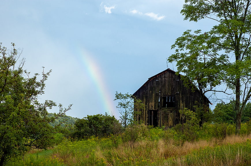 Old weathered wooden barn with rainbow in rural landscape