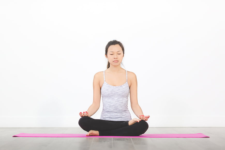 Woman meditating in lotus pose on pink yoga mat