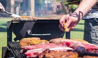 Close-up of hands seasoning meat on outdoor grill