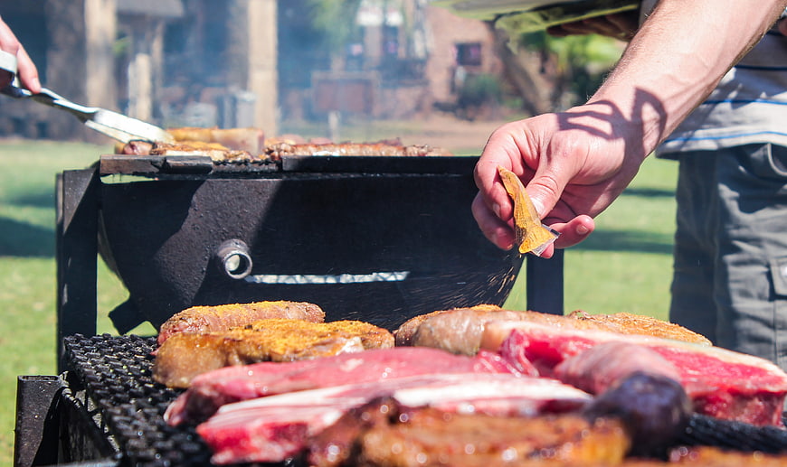 Close-up of hands seasoning meat on outdoor grill