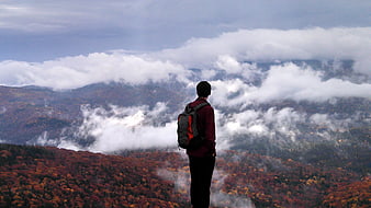 Hiker with backpack overlooking autumn mountains and clouds