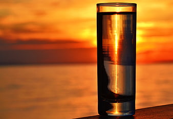 Glass of Water with Sunset Reflection on Wooden Surface