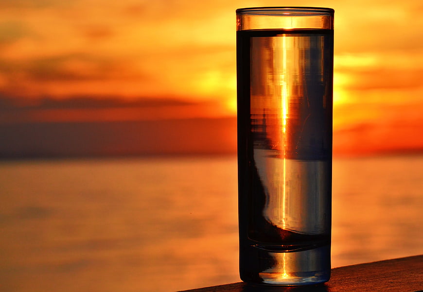 Glass of Water with Sunset Reflection on Wooden Surface