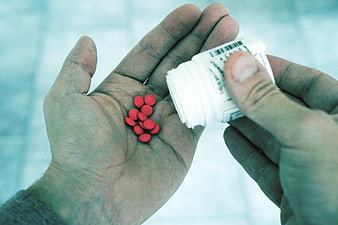 Hands Pouring Red Pills from White Medicine Bottle
