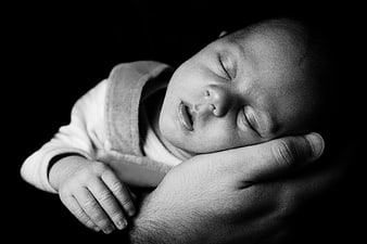 Black and white portrait of a sleeping newborn baby held by an adult hand