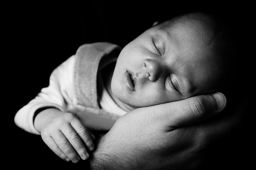 Black and white portrait of a sleeping newborn baby held by an adult hand