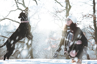 Happy Woman Playing with Black Dog in Snowy Winter Forest