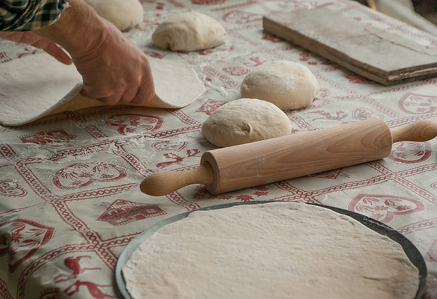 Hands Rolling Out Dough on Patterned Tablecloth
