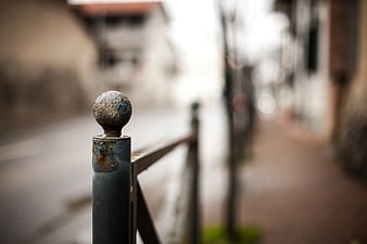 Close-up of Rusty Metal Fence Post with Blurred Street Background