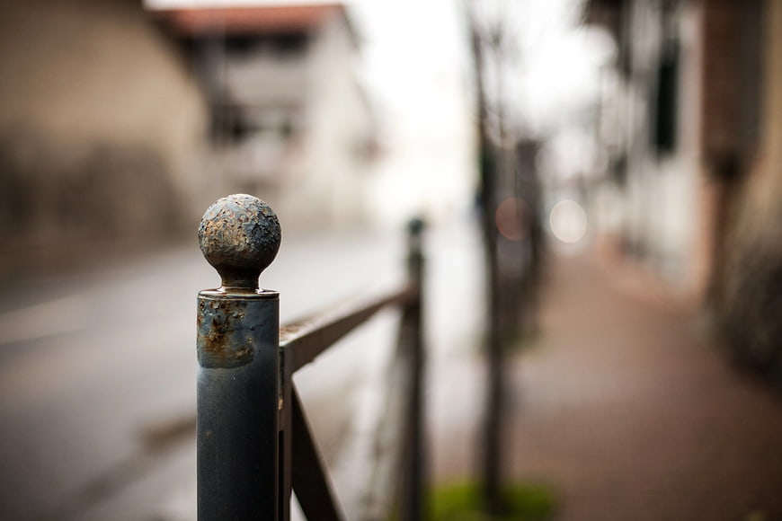 Close-up of Rusty Metal Fence Post with Blurred Street Background