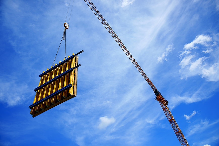 Yellow Construction Formwork Suspended by Crane Against Blue Sky